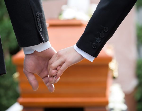 Religion, death and dolor - couple at funeral holding hands consoling each other in view of the loss